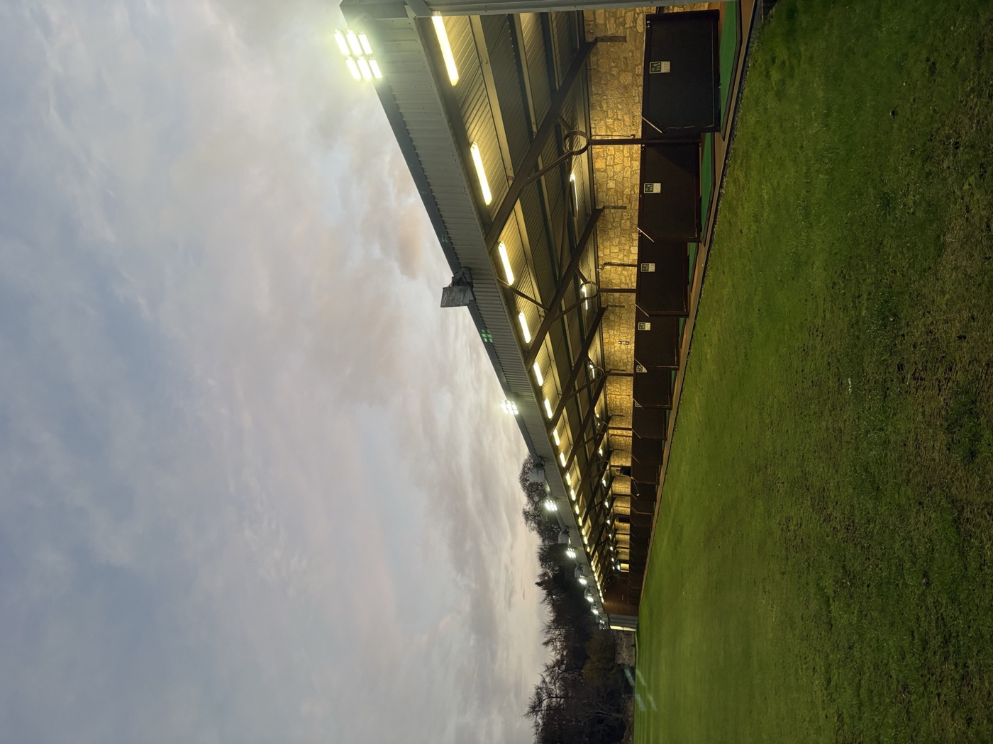 Covered driving range bays at Kings Acre at dusk, floodlights on
